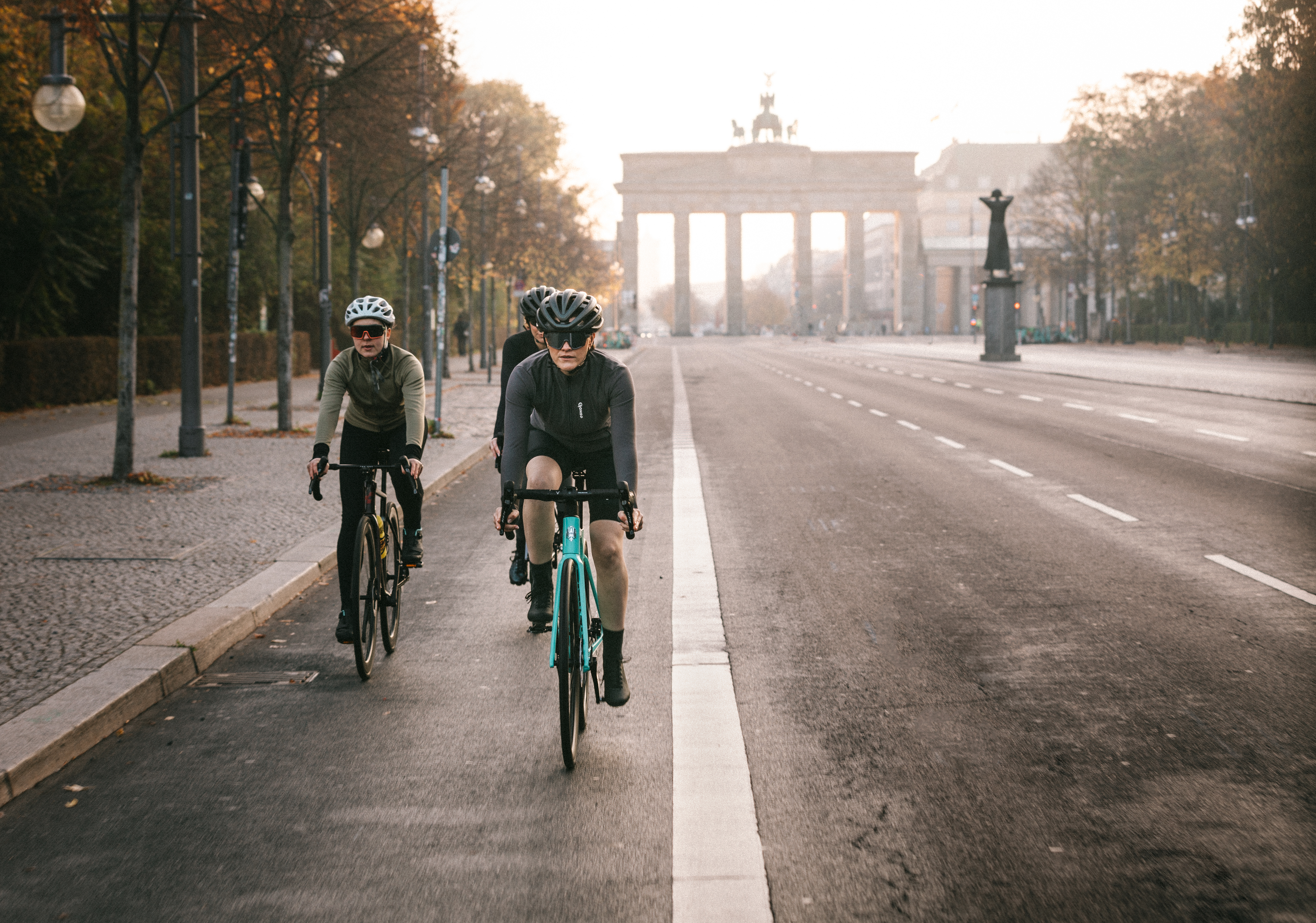 Three cyclists ride along an empty road toward the Brandenburg Gate early in the morning.
