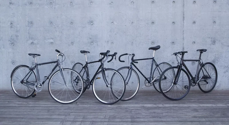 Five bikes are standing side by side in front of a gray concrete wall on a wooden floor.