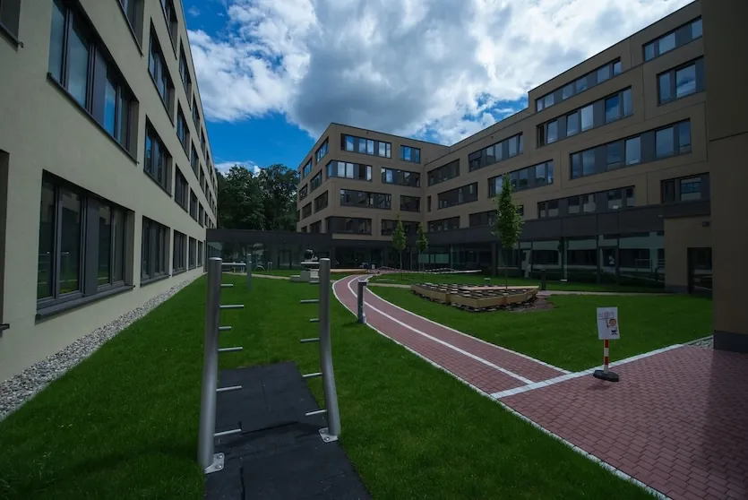 A modern office complex with a green courtyard, running track, and outdoor fitness equipment.