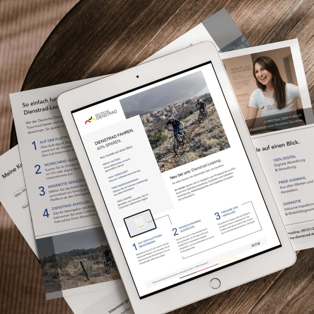 A tablet is lying on a table, displaying a page about "company bike leasing." Brochures containing information about company bike leasing are laid out under the tablet. One of the brochures features a photo of a woman named "Christina Diem-Puello."