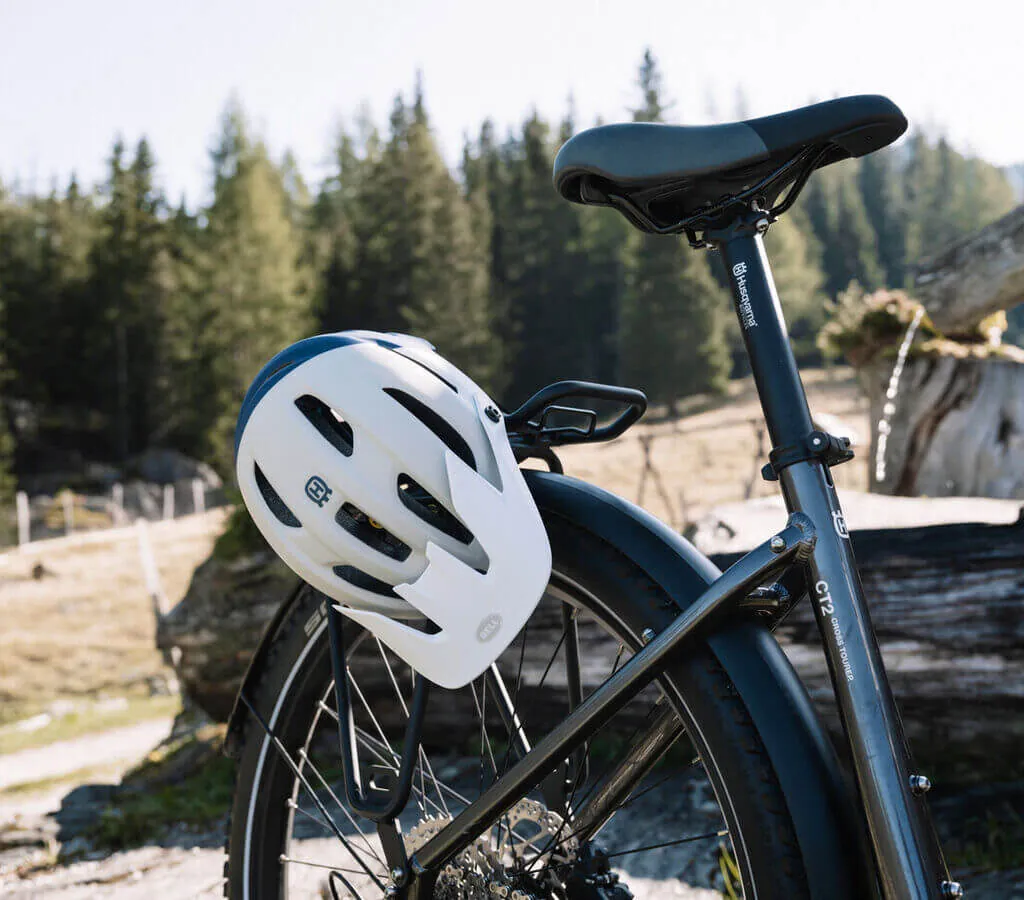 A white bicycle helmet hangs on the saddle of a black bike standing in a wooded landscape.