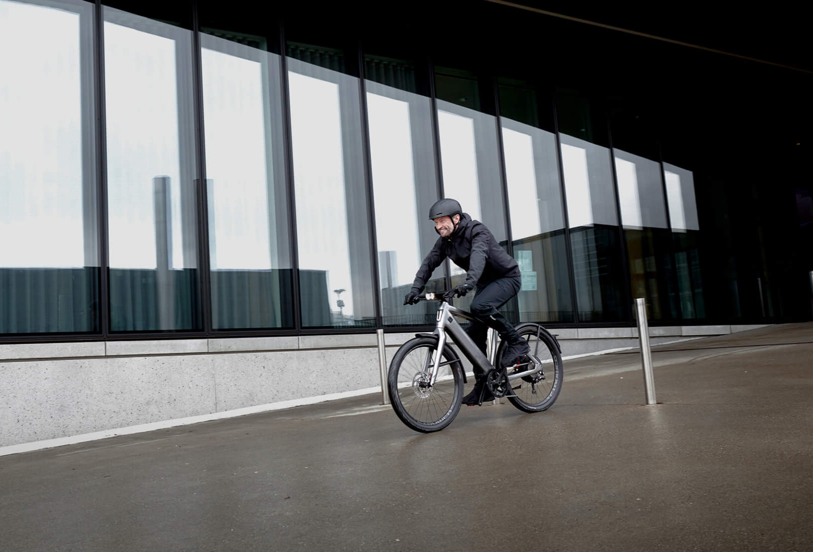 Eine Person fährt ein E-Bike auf einem nassen Boden vor einem modernen Gebäude mit großen Glasfenstern.