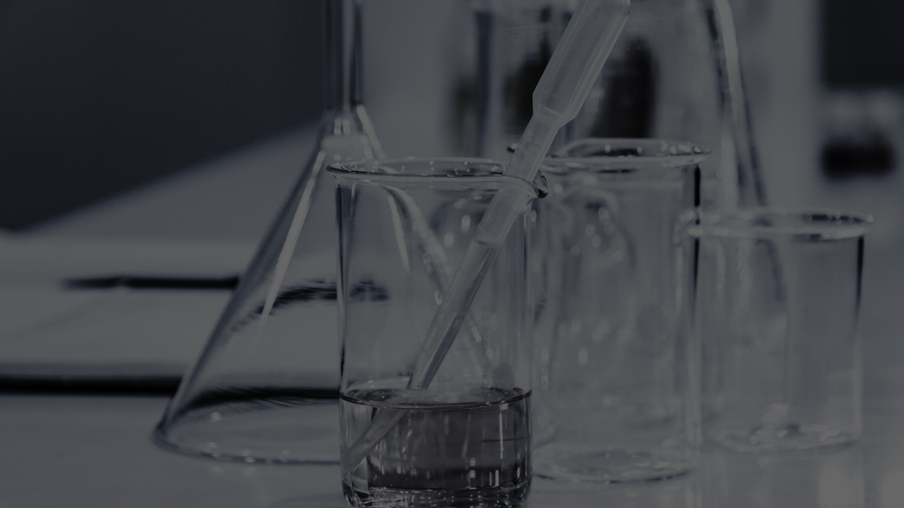 Close-up of glass containers and a pipette in a laboratory setting, partially filled with liquid. The scene appears calm and focused on laboratory work.