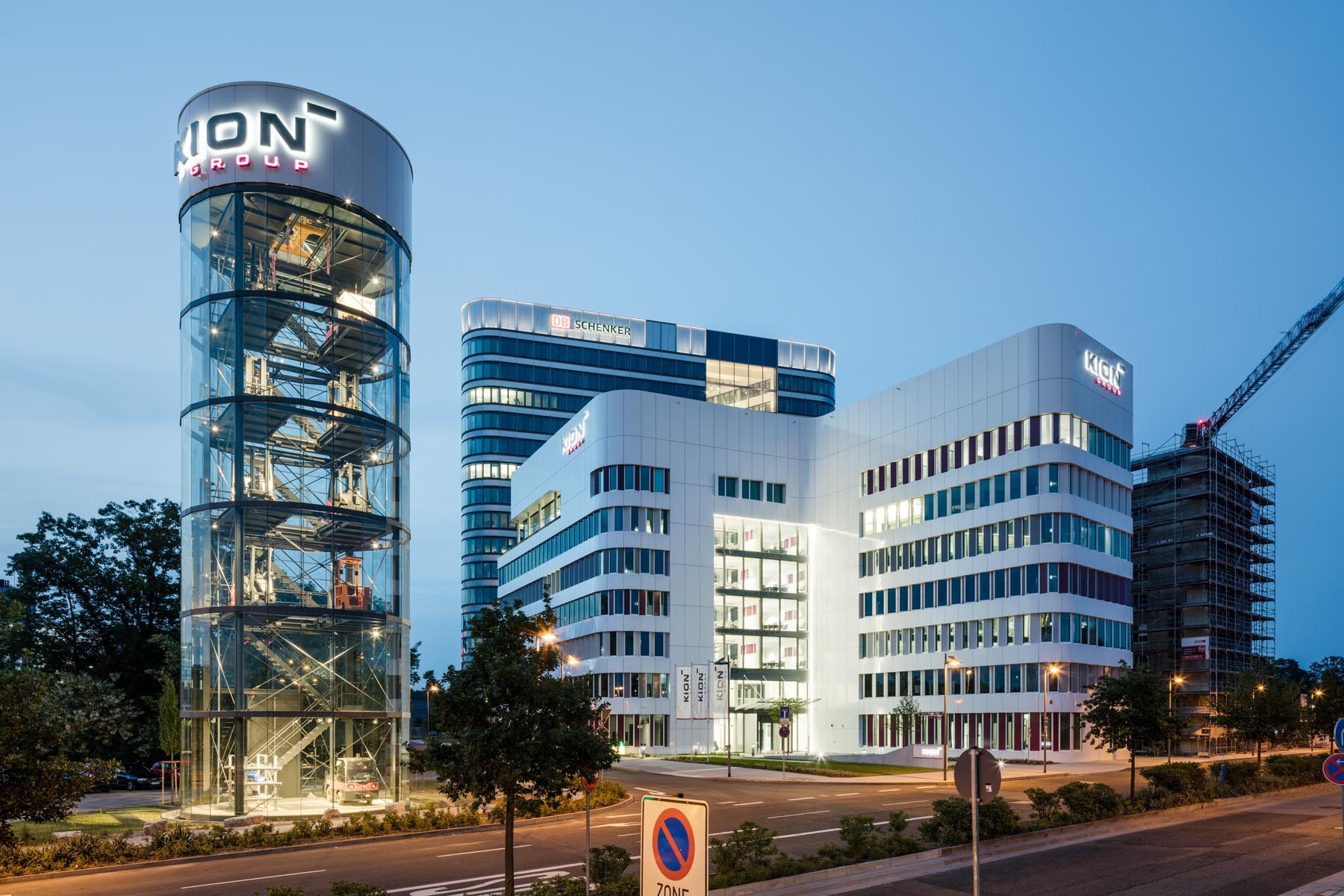 Modern office buildings at dusk, with a round glass tower on the left and several tall buildings in the background.